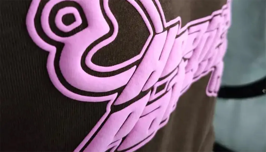 Stylish Puff Print Hoodies for Cozy Warmth and Trendy Look 1 Close-up of pink embroidered logo on fabric.