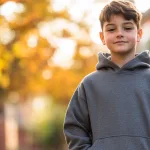 A young boy wearing an oversized hoodie, standing confidently in an urban park setting.