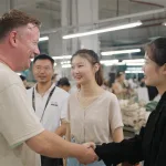 Brand owner and Ninghow Apparel team shaking hands in front of the production floor.
