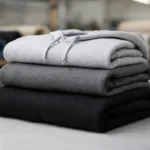 A side-by-side display of 10 oz, 12 oz, and 16 oz hoodies on a manufacturing table, visually comparing thickness and texture for buyers.