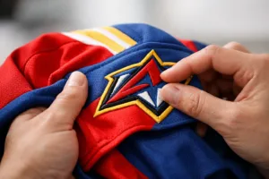 Home 42 A detailed scene showing hand inspection of a team jersey's stitching, fabric texture, and logo embroidery, demonstrating practical QC techniques.